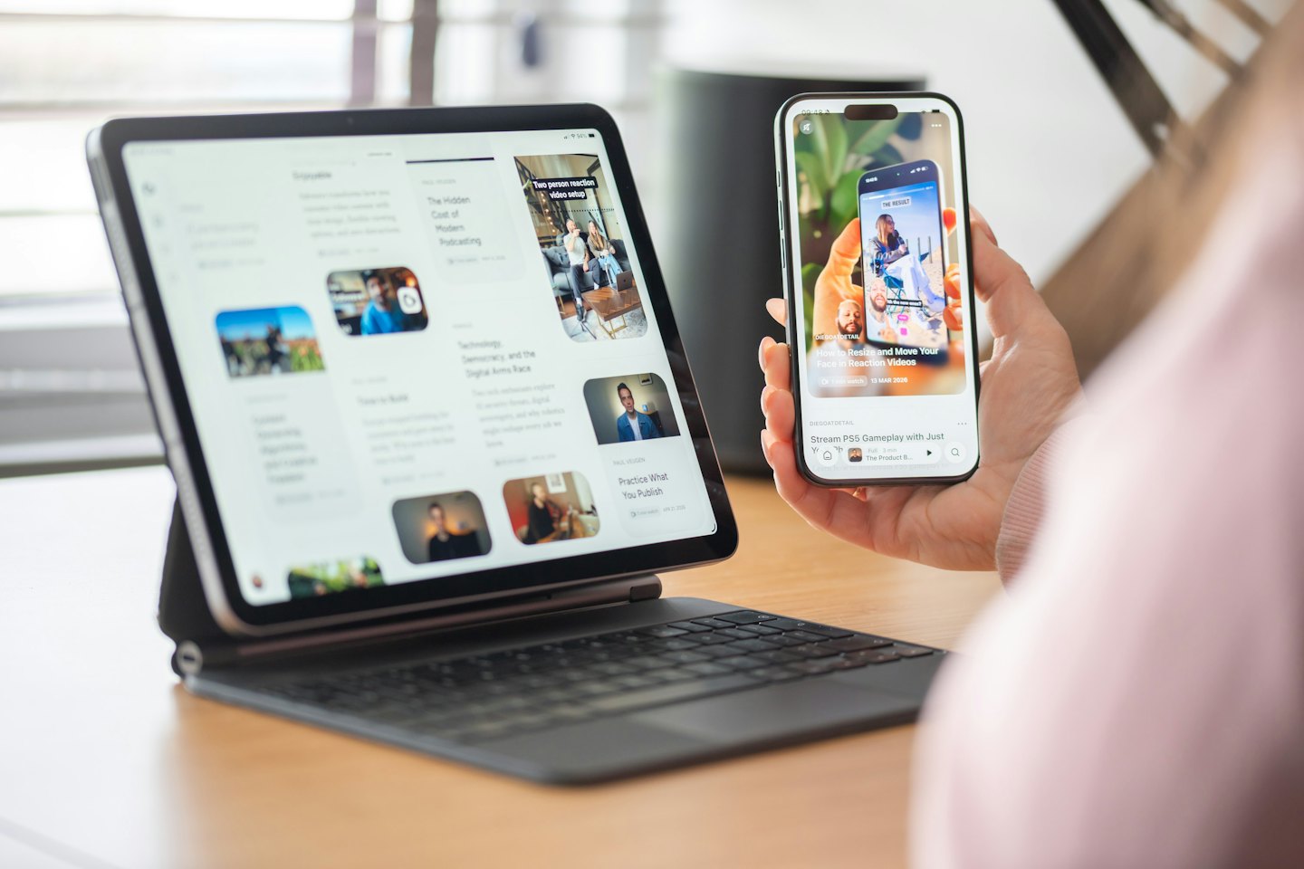 Mani che tengono uno smartphone e un tablet su una scrivania di legno.