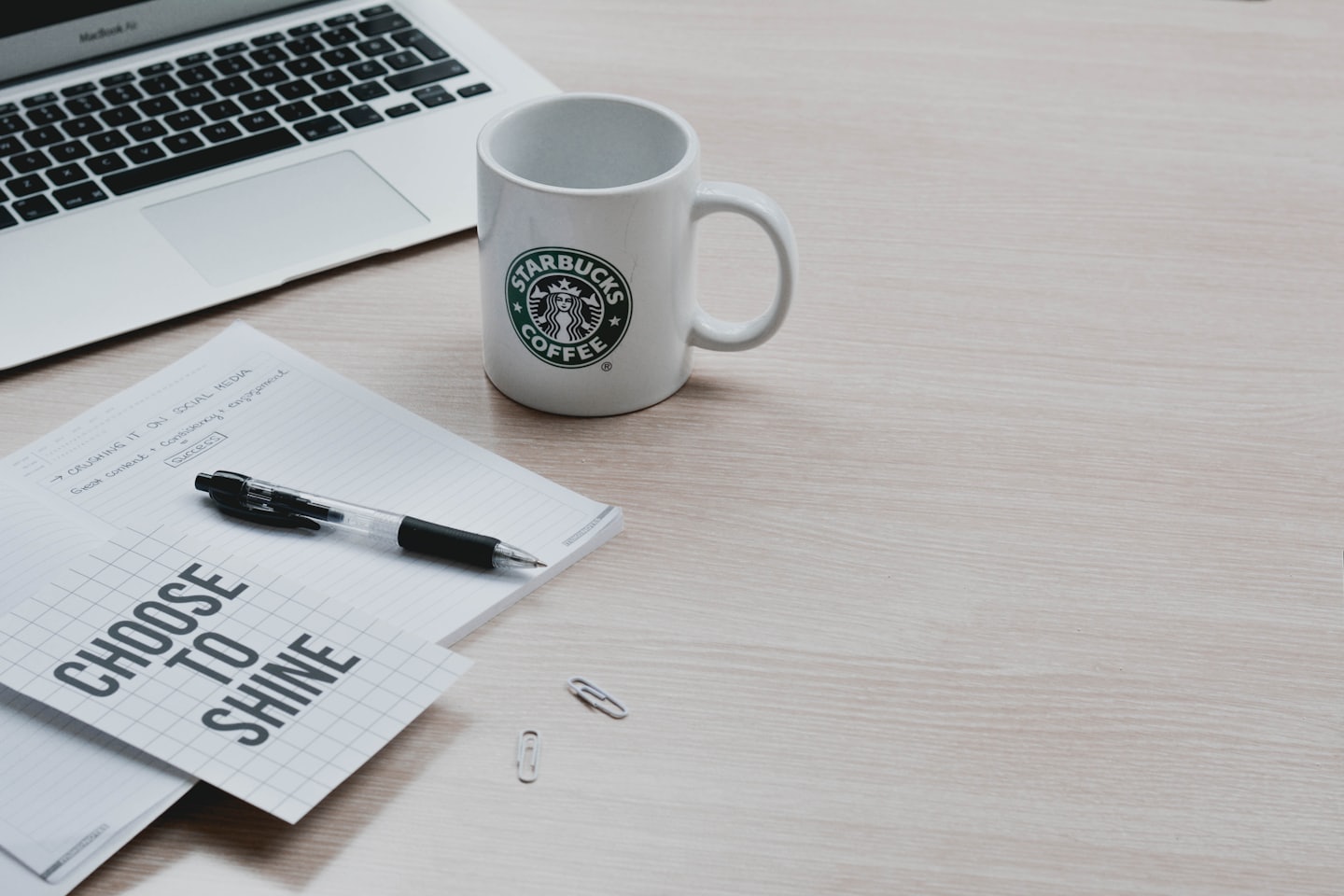 Un laptop, un taccuino e una tazza di caffè su una scrivania.