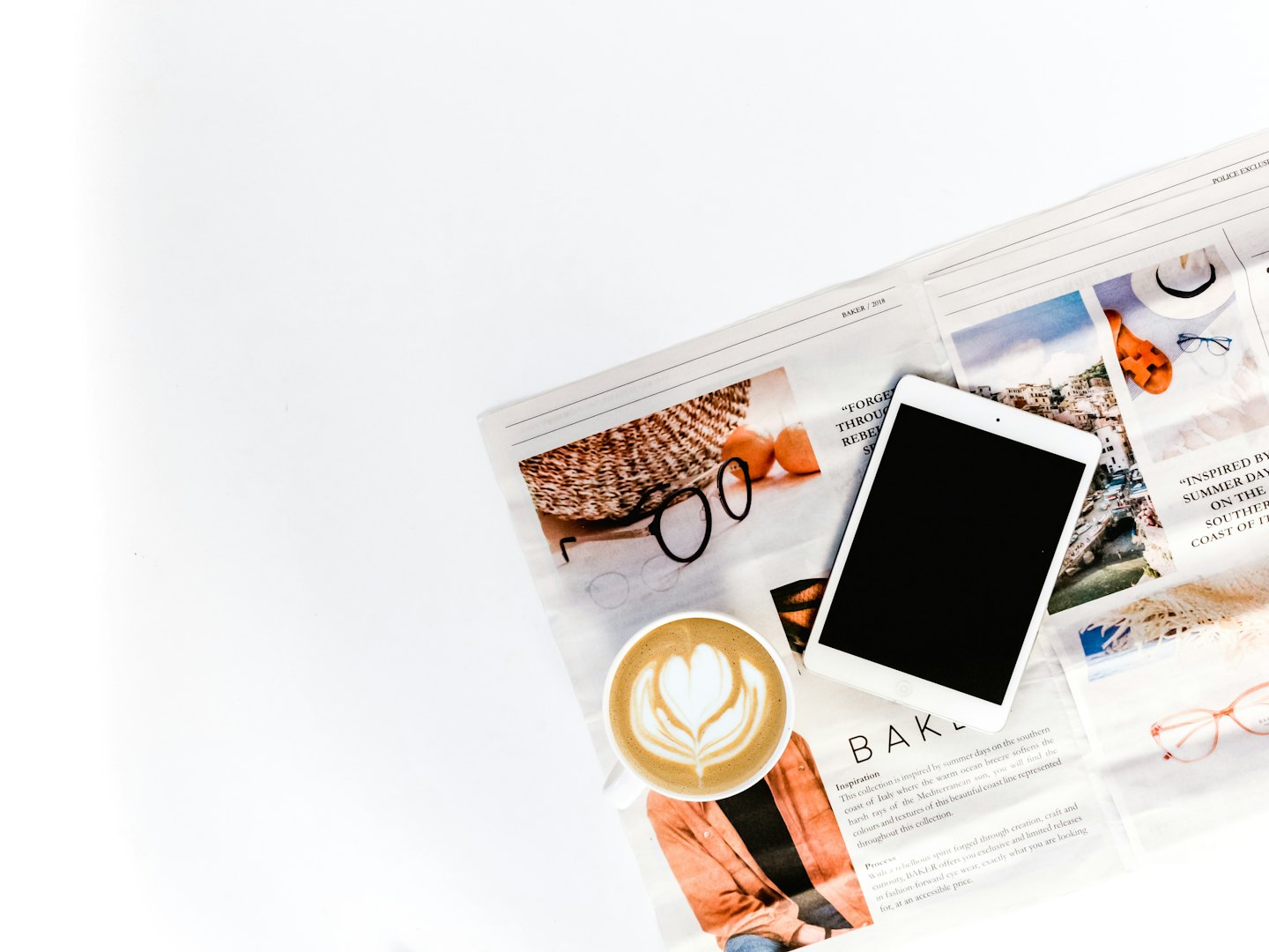 Tablet, cappuccino con decorazione e rivista aperta sul tavolo.